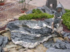 Harasimowicz ogrody - Figura z brązu - chłopiec w kapeluszu siedzący na kamieniu